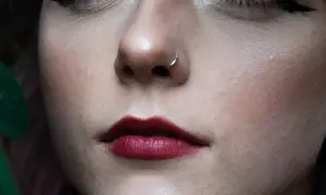 Delikatny nostril z małym kółkiem błyszczy na tle pełnych, malinowych ust.