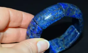 Błękitna bransoleta z lapis lazuli, ozdobiona złotymi inkluzjami, spoczywa na dłoni.
