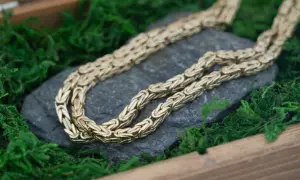Złota keta o skomplikowanym splocie spoczywa na kamieniu, otoczona zielonym mchem.