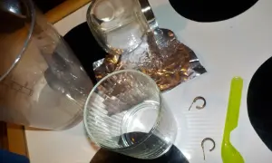 Srebrne kolczyki, folia aluminiowa, sól i szklanka na stole.