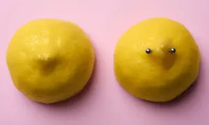 Dwa cytryny na różowym tle. Jedna z nich ma kolczyk w sutku, cena tego zabiegu może być różna.