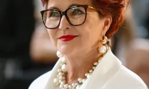 Elegancka kobieta w okularach i bogatej biżuterii z pereł. Pokazuje, jak nosić perły, by wyglądać szykownie.