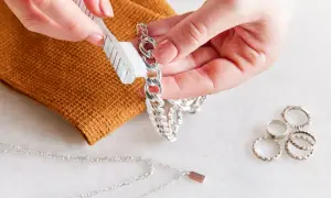 Delikatne czyszczenie srebrnego łańcuszka szczoteczką. Obok leżą inne pierścionki i naszyjnik.