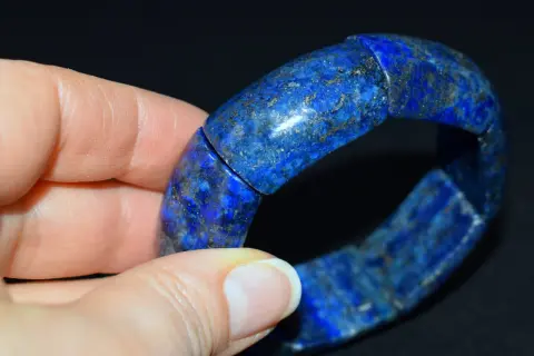 Błękitna bransoleta z lapis lazuli, ozdobiona złotymi inkluzjami, spoczywa na dłoni.
