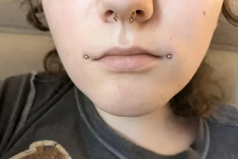 Dwa kolczyki dahlia piercing zdobią usta, dodając odważnego charakteru.