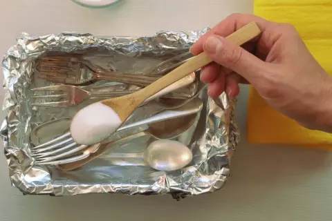 Srebrne sztućce w folii aluminiowej, na łyżce soda oczyszczona.