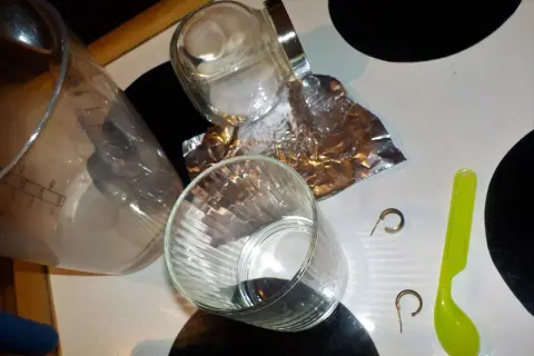 Srebrne kolczyki, folia aluminiowa, sól i szklanka na stole.