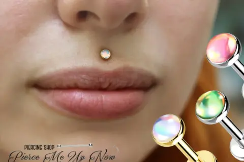 Delikatny, opalizujący center labret na ustach. W tle błyszczące ozdoby do piercingu.