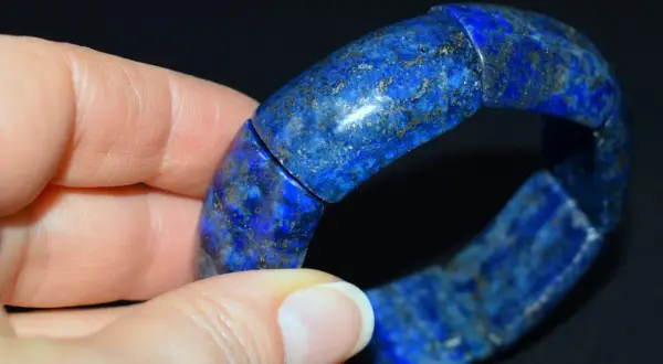 Błękitna bransoleta z lapis lazuli, ozdobiona złotymi inkluzjami, spoczywa na dłoni.