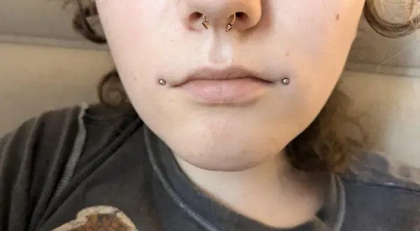 Dwa kolczyki dahlia piercing zdobią usta, dodając odważnego charakteru.