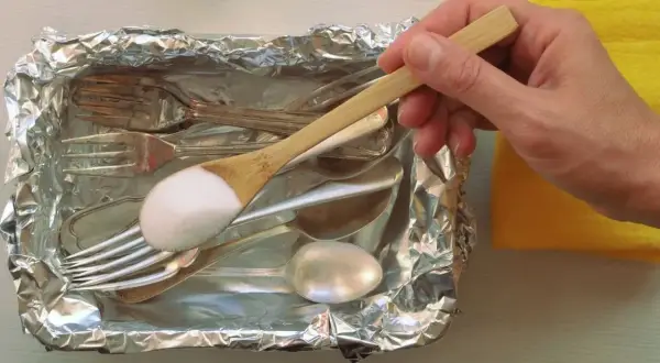 Srebrne sztućce w folii aluminiowej, na łyżce soda oczyszczona.