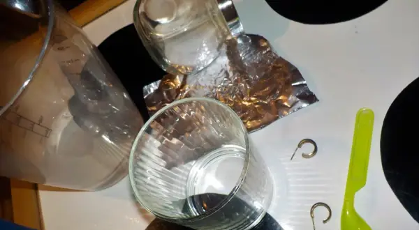 Srebrne kolczyki, folia aluminiowa, sól i szklanka na stole.