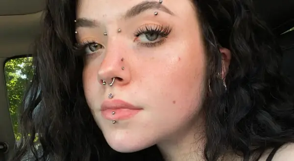 Młoda kobieta z wieloma kolczykami, w tym kolczyk w brwi, septum i wargach.
