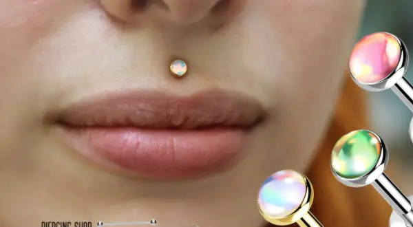 Delikatny, opalizujący center labret na ustach. W tle błyszczące ozdoby do piercingu.