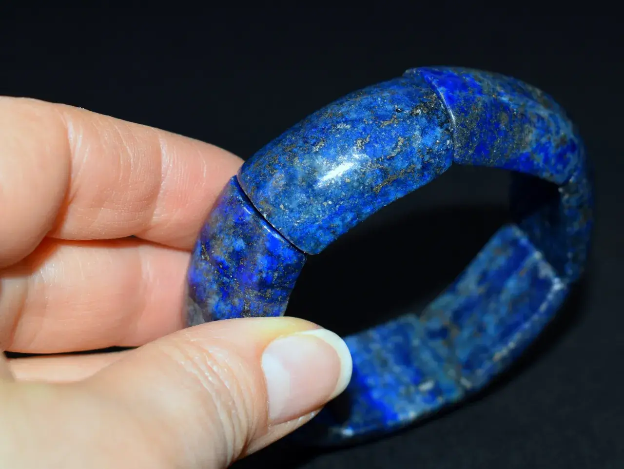 Błękitna bransoleta z lapis lazuli, ozdobiona złotymi inkluzjami, spoczywa na dłoni.