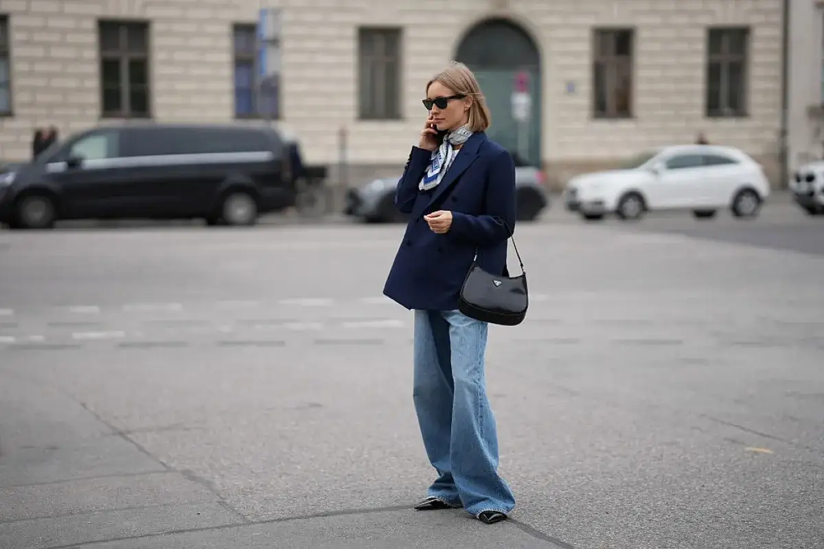 Elegancka kobieta w granatowej marynarce i jeansach pokazuje, jak nosić perły, dodając szyku codziennej stylizacji.