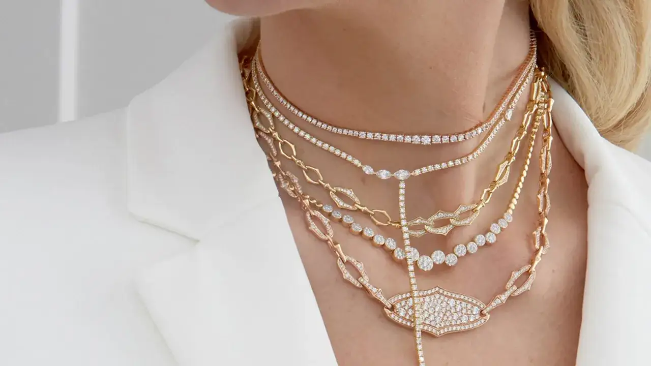 Elegancka kobieta pokazuje, jak nosić kilka łańcuszków, tworząc bogatą, lśniącą kompozycję z diamentów i złota.
