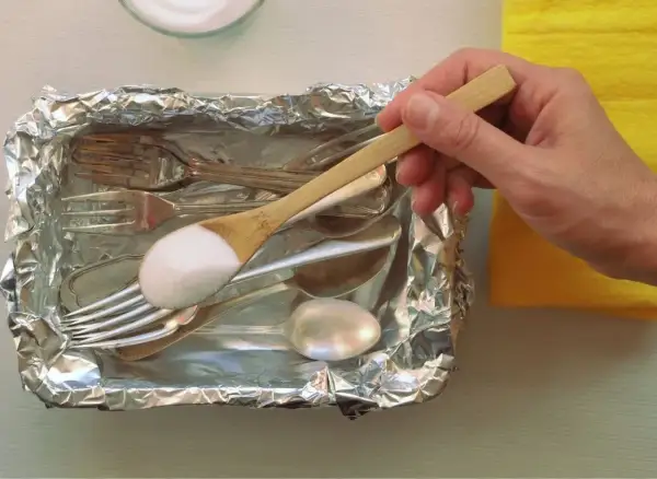 Srebrne sztućce w folii aluminiowej, na łyżce soda oczyszczona.
